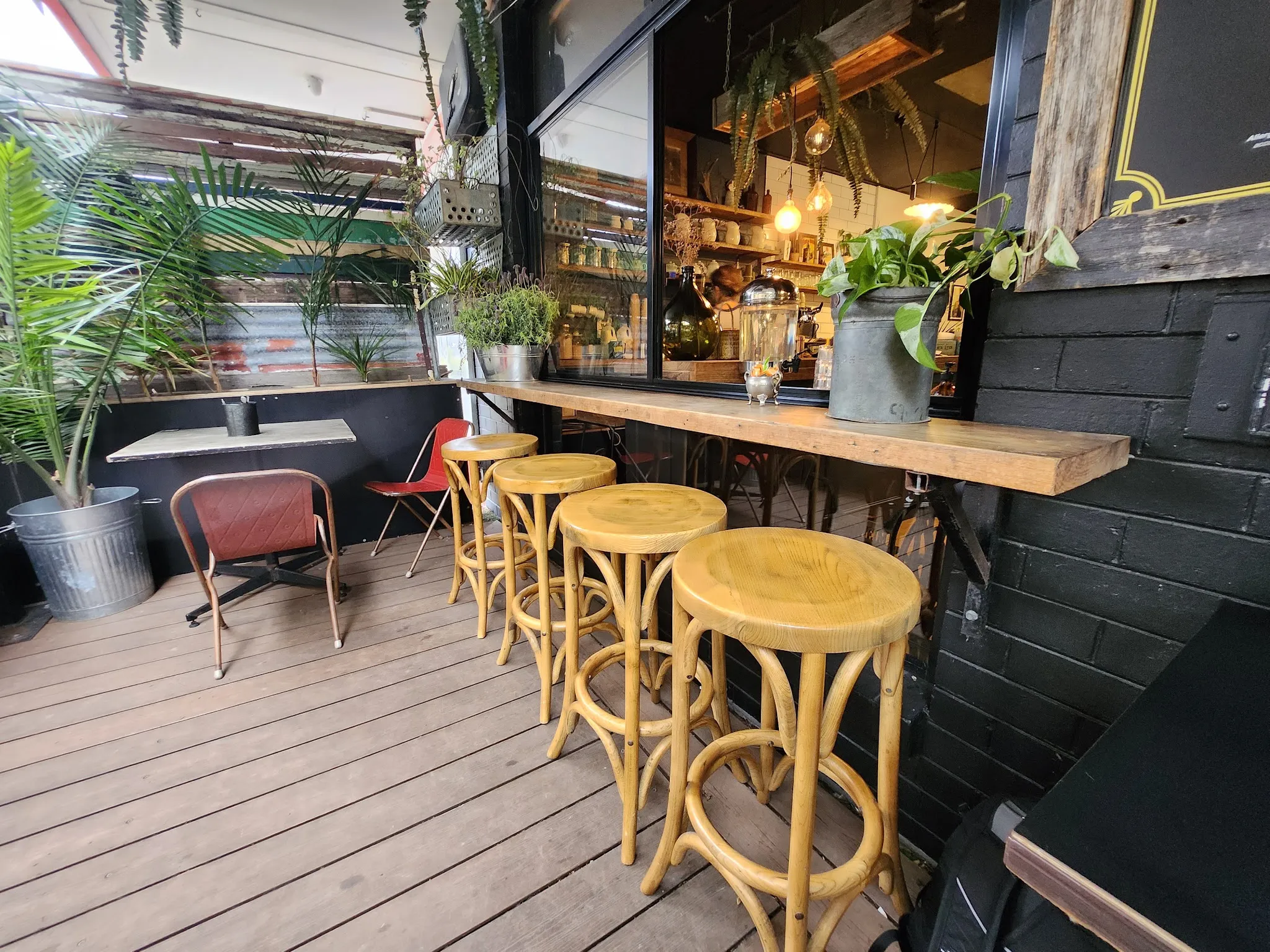 Fork And Waffle Cafe outdoor deck with yellow bamboo stools, lush potted tropical plants, and the warm interior visible through the window