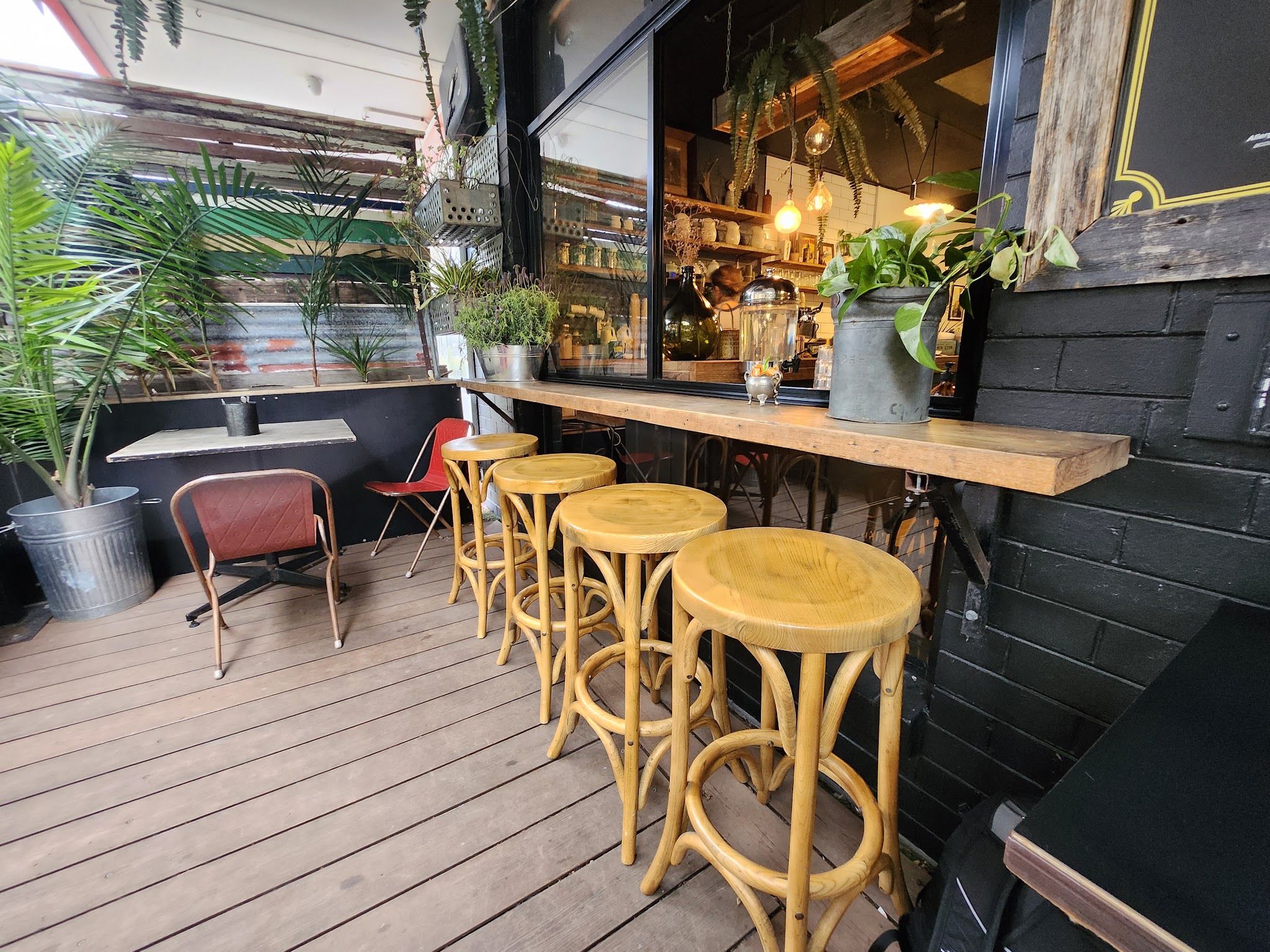 Fork And Waffle Cafe outdoor deck with yellow bamboo stools, plants, and warm interior visible through window