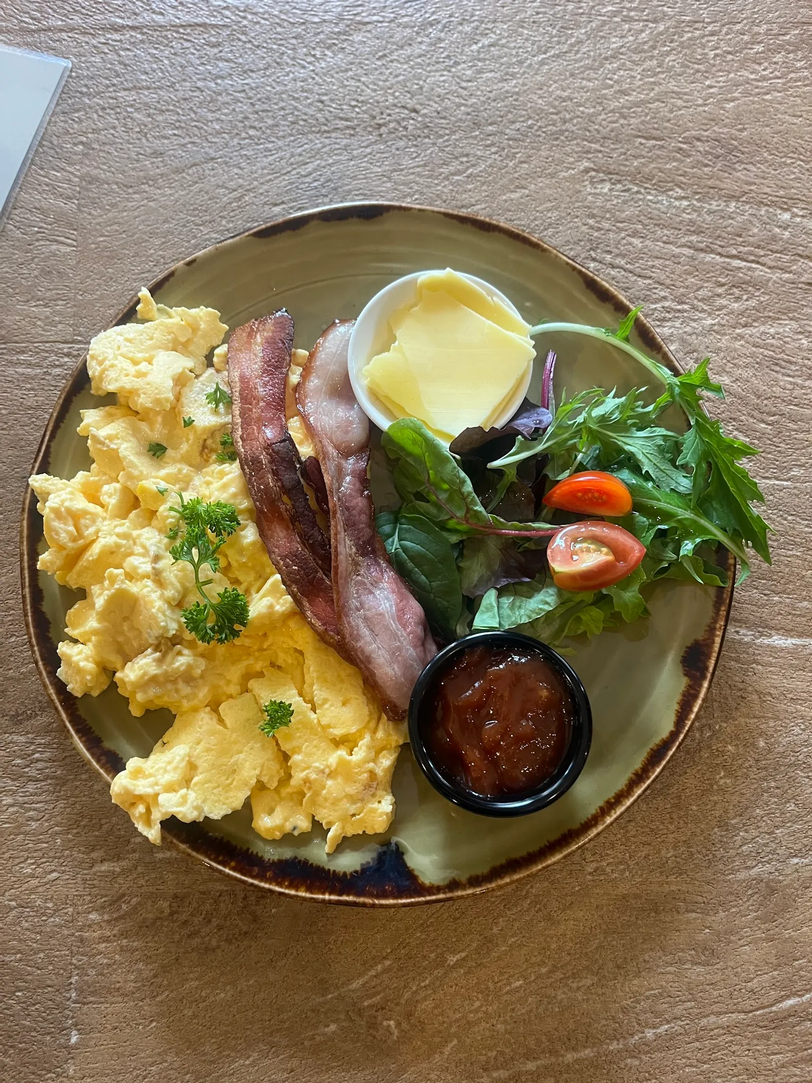 Overhead breakfast plate with scrambled eggs, bacon, salad and relish on artisan ceramic