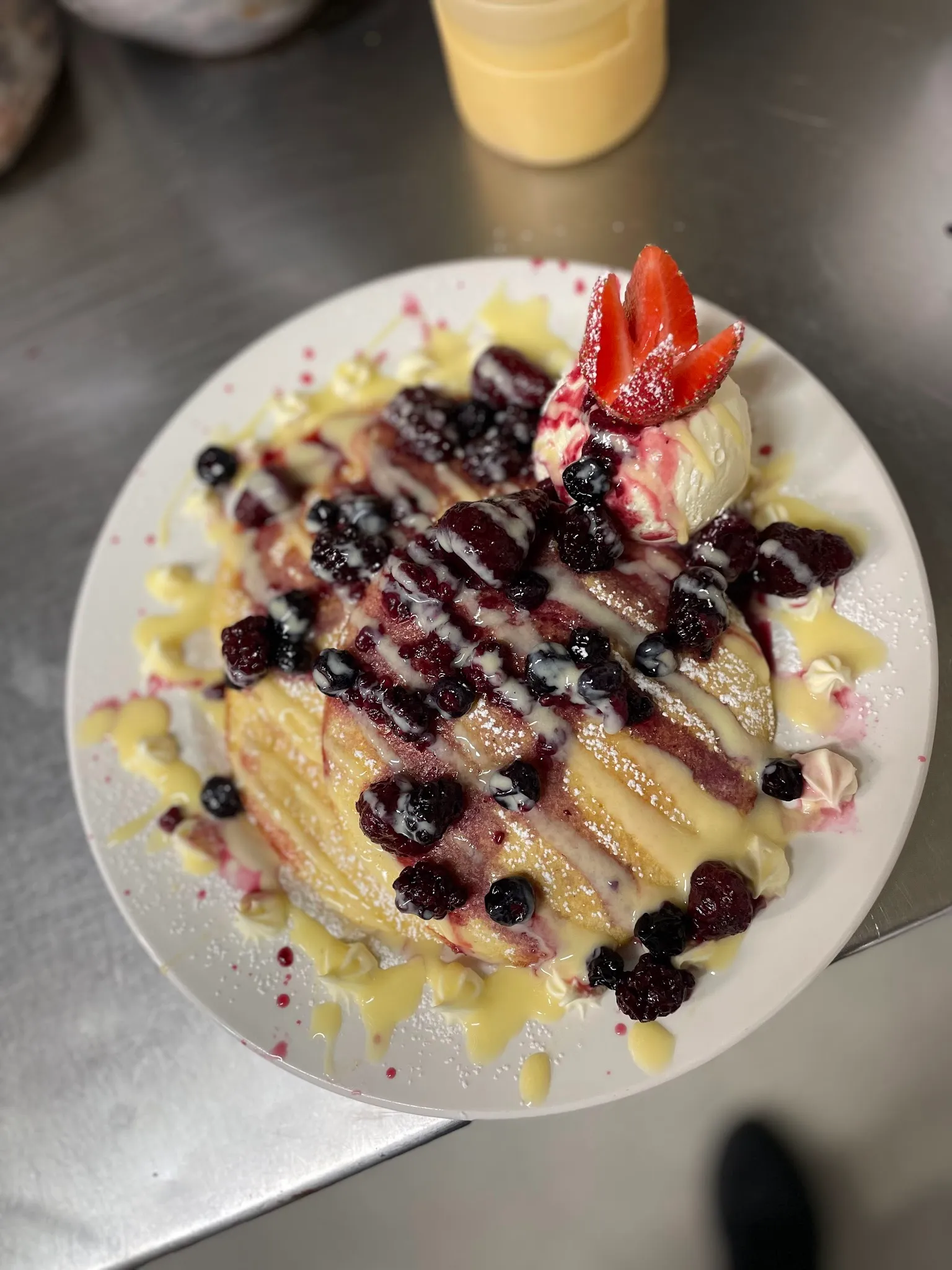 Overhead berry crepes with custard drizzle, a scoop of ice cream and fresh strawberry on a white plate