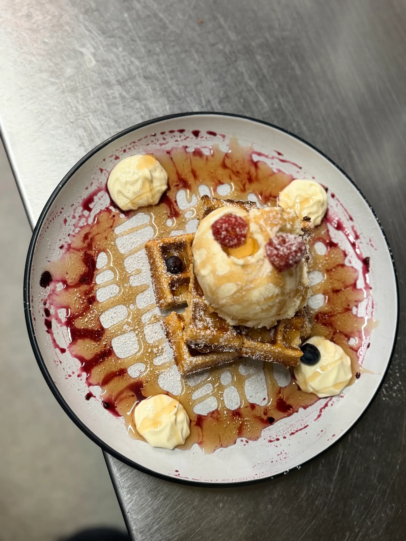 Belgian waffle with vanilla ice cream, caramel sauce and cream rosettes on a decorative white plate