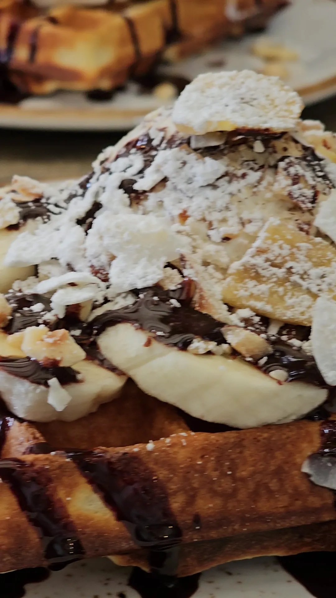 Close-up Belgian waffle loaded with Nutella drizzle, sliced banana, crushed nuts and whipped cream
