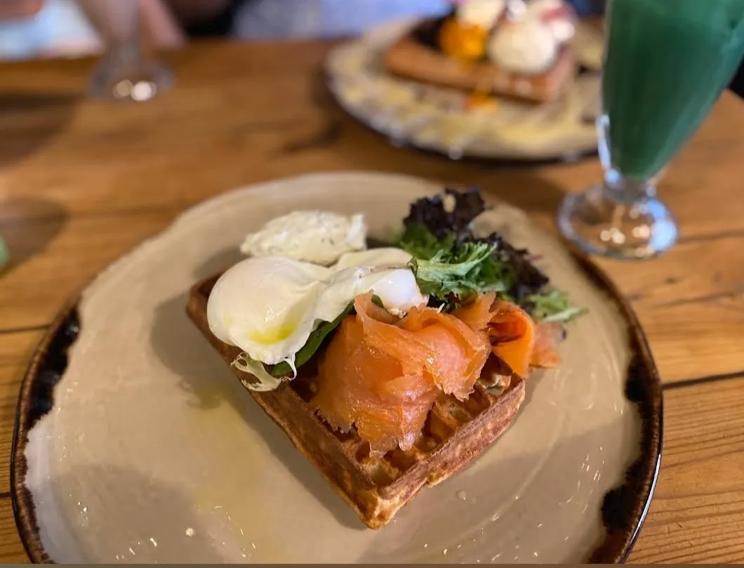Savoury waffle with smoked salmon and poached egg on ceramic plate, with other dishes visible on dining table