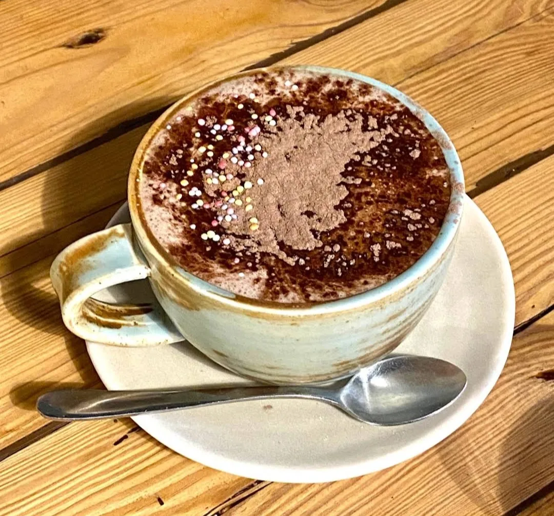 Artisan ceramic mug of hot chocolate with cocoa dusting and sprinkles on a warm blonde timber table