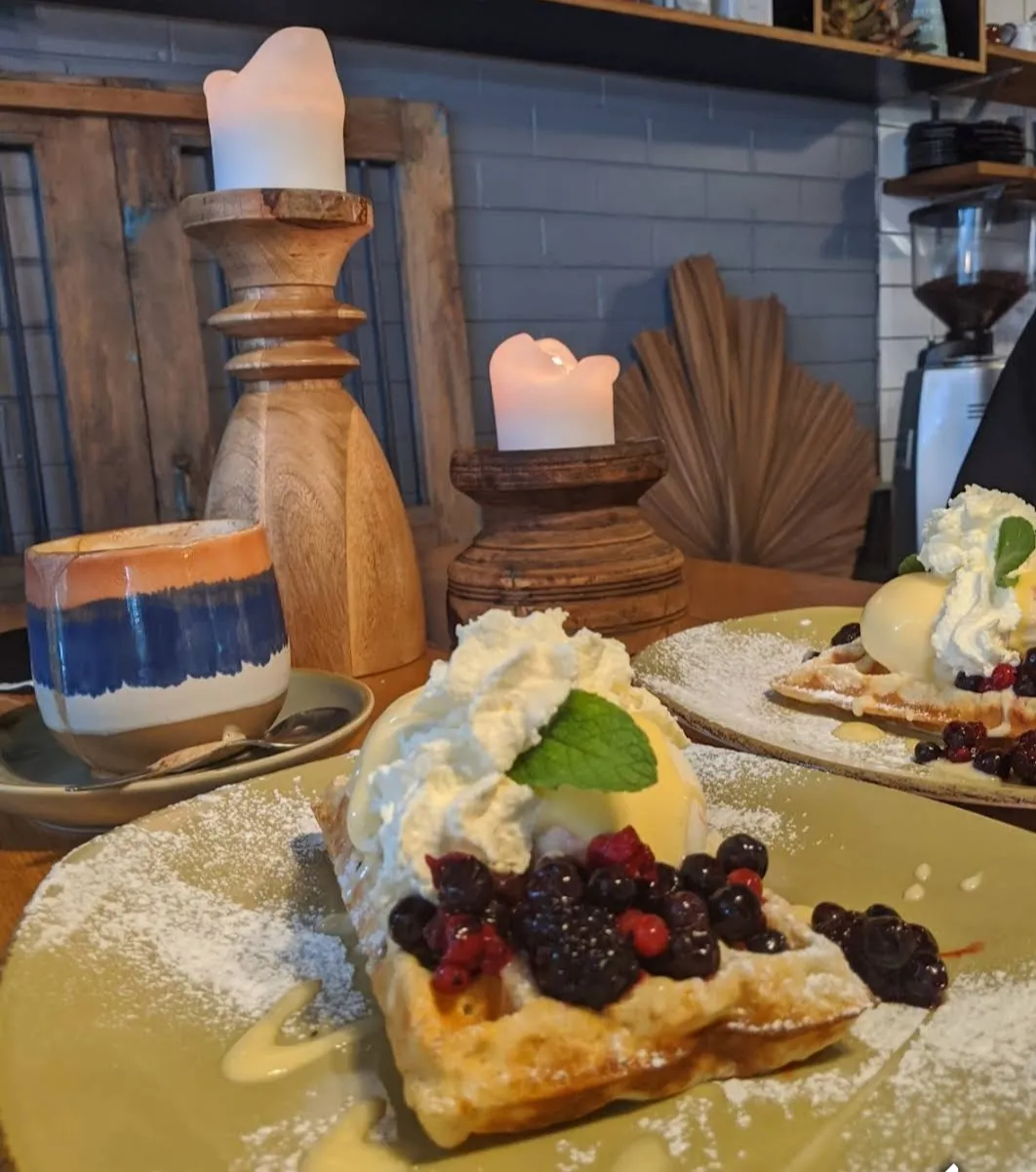 Waffle with mixed berries, ice cream and mint on sage plate, with candles and cafe interior behind