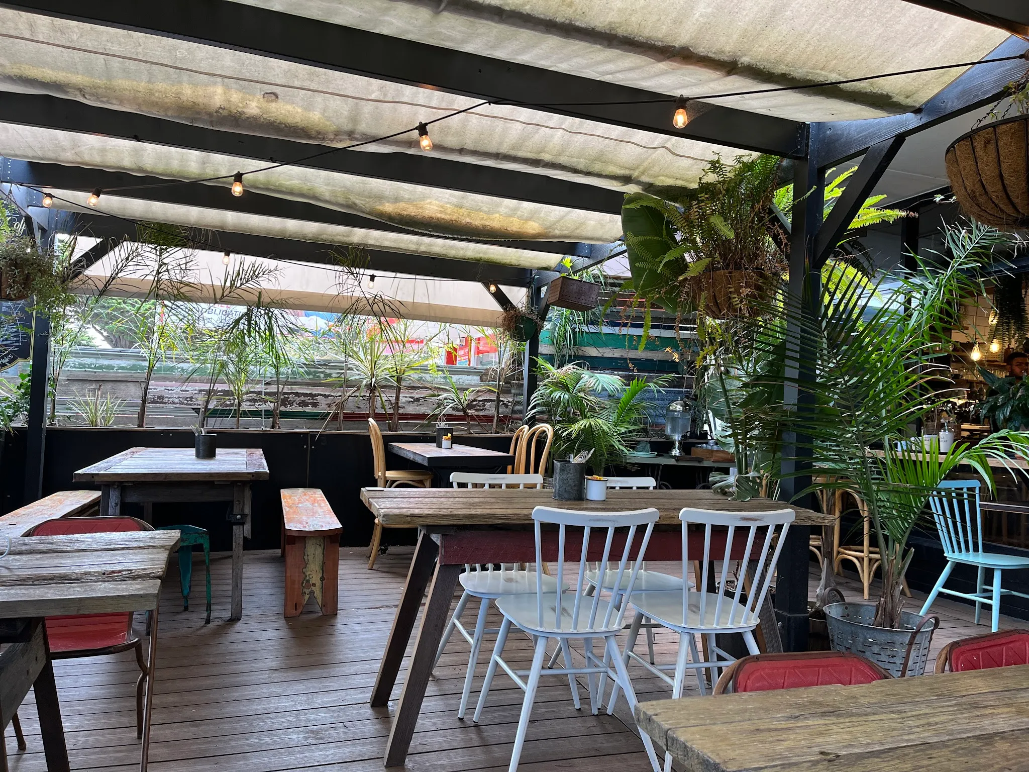 Fork And Waffle Cafe covered outdoor terrace with festoon lights, tropical plants and mismatched chairs