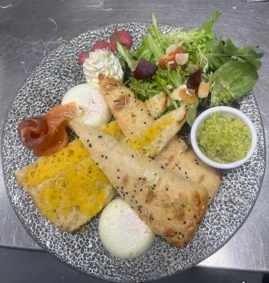 Elaborate brunch plate with smoked salmon, poached eggs, flatbread, salad and pesto on textured grey ceramic