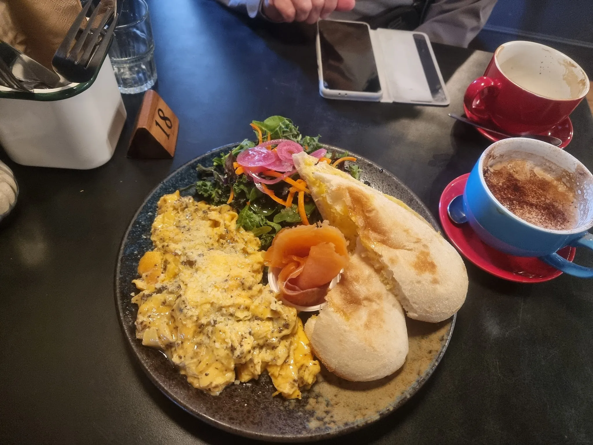 Scrambled egg and smoked salmon brunch plate on dark blue ceramic alongside two colourful coffee cups on a dining table