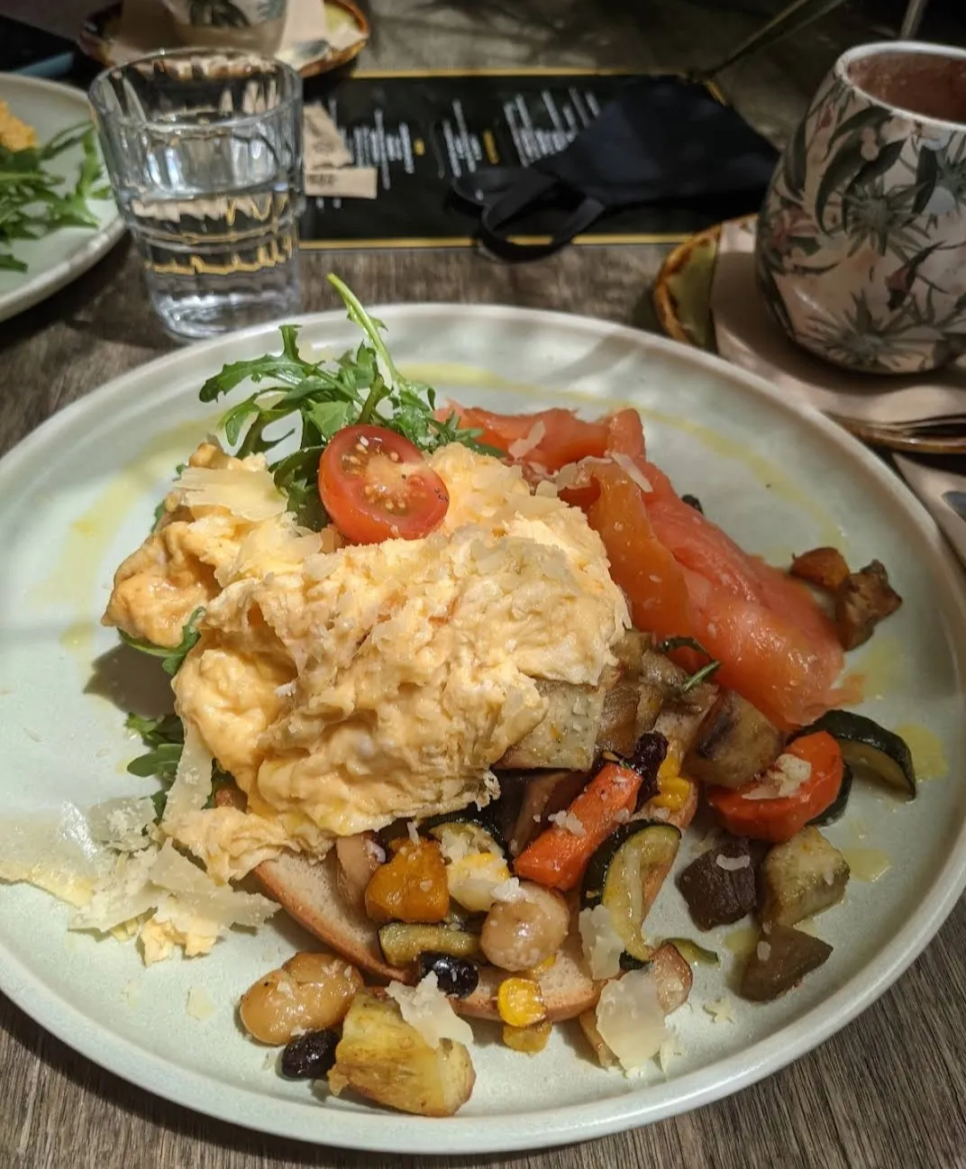 Scrambled eggs with roasted vegetables, smoked salmon and shaved parmesan on a white plate at a dining table