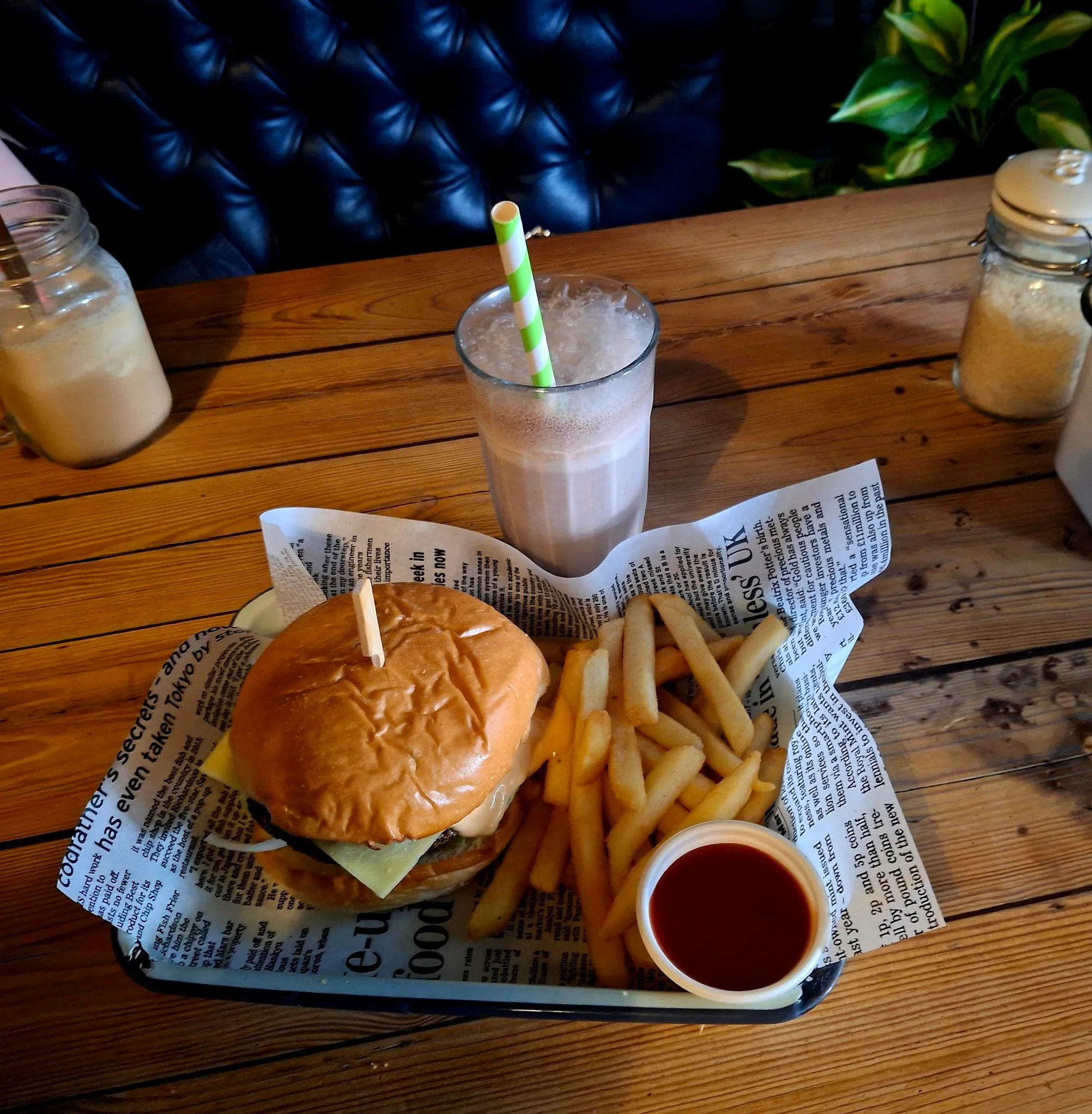 Cheeseburger and chips on a black tray with a milkshake on timber table in front of a tufted leather booth