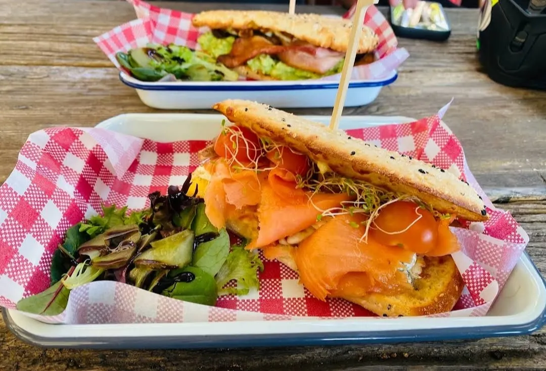 Two smoked salmon flatbread rolls on red-check wax paper in enamel trays on a timber table
