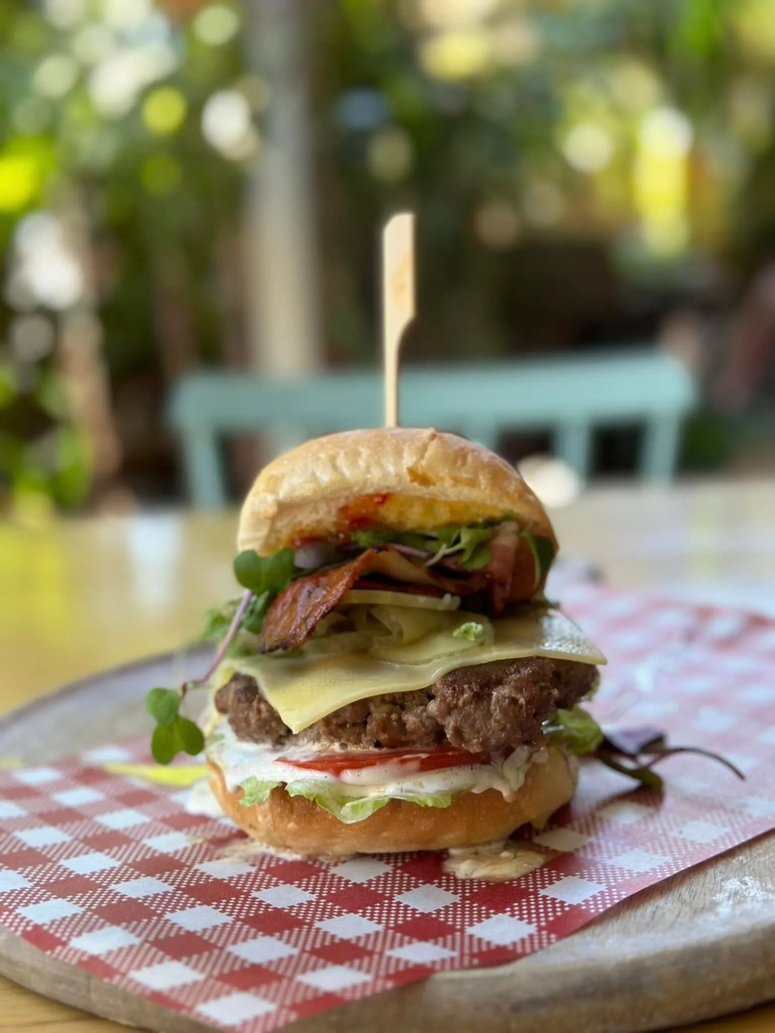 Stacked gourmet burger on red-check board with garden bokeh background