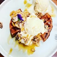 Belgian waffle with vanilla ice cream, honey drizzle, crushed walnuts and an edible purple flower on a white plate